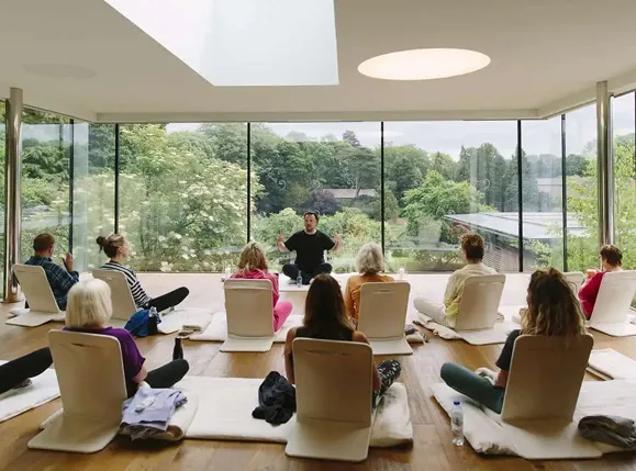 Retreat participants seated in a meditation session in a glass-walled room overlooking gardens